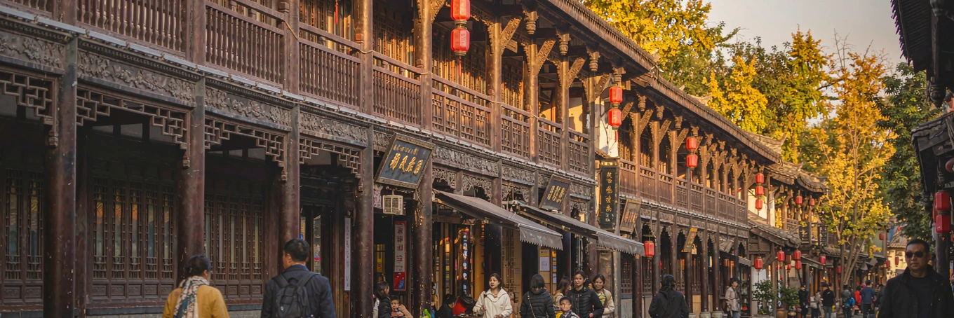 宽窄巷子街区入口石牌坊与傍晚暖光，传统青砖与远处现代楼群对比